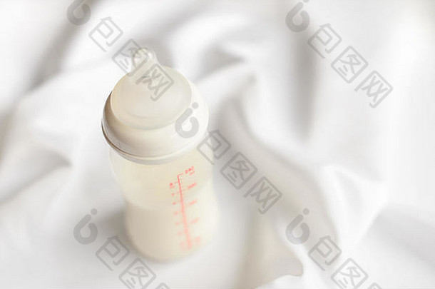 在白色丝绸缎子背景上为新生儿提供一瓶牛奶。免费拷贝空间。妇幼保健概念。