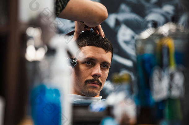 男人在理发店剪时髦发型的特写镜头。男发型师为客户服务，使用机器和梳子理发。