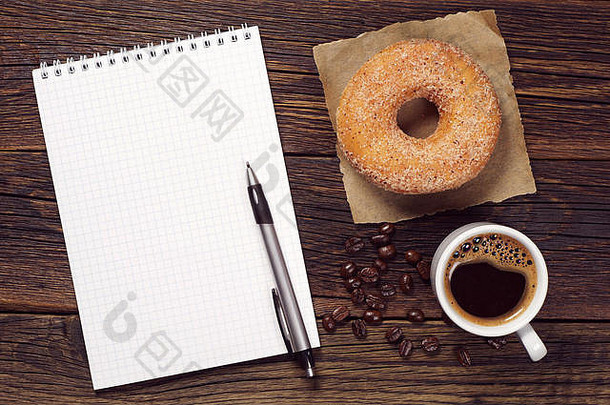 笔记本和一杯带甜甜圈的热咖啡放在旧木桌上，俯视图