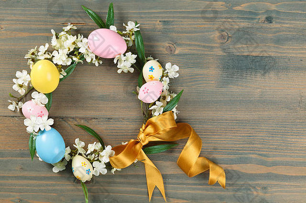 五颜六色的复活节彩蛋和春天的鲜花组成的花环。在质朴的木制背景上。