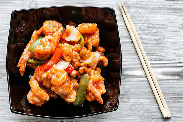 <strong>韩国料理</strong>-木桌上黑色碗中的腰果炒虾和糖醋酱蔬菜（虾组合）的俯视图