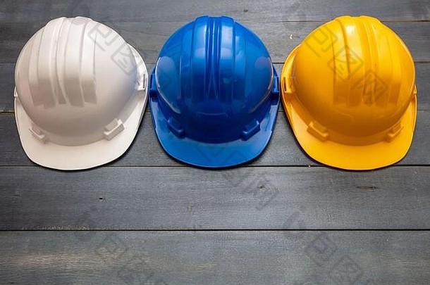 安全生产防护设备。工业防护安全帽木质背景上的白色、黄色和蓝色。个人健康和安全概念