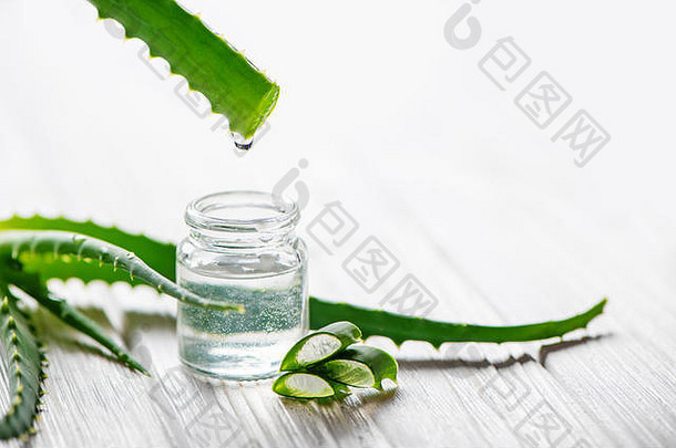 白色木质背景上的新鲜芦荟叶和芦荟汁玻璃罐。自然医学概念。