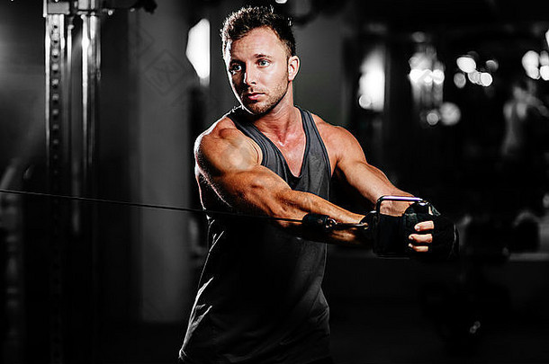 英俊的健美运动员在黑色背景的健身房里锻炼身体