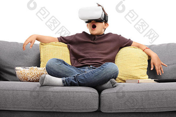 震惊孩子虚拟现实护目镜坐着沙发孤立的白色背景