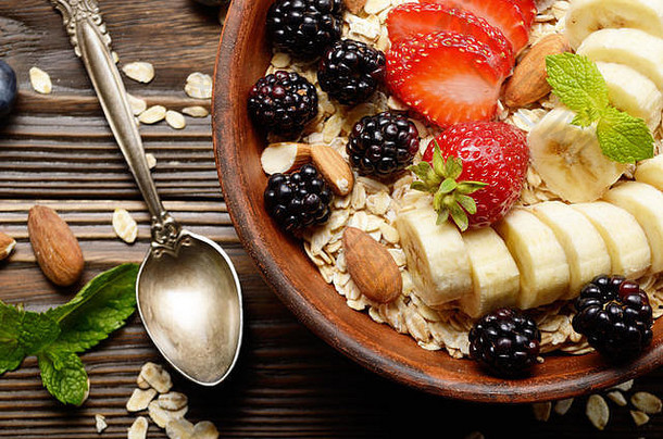在木制厨房桌子上的粘土盘中，可以俯瞰水果健康的慕斯丽，香蕉、草莓、杏仁和黑莓