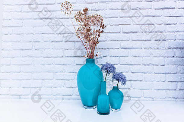 绿松石花瓶里的野花站在白色的桌子上，靠着白色的路缘墙。花瓶里的野花。