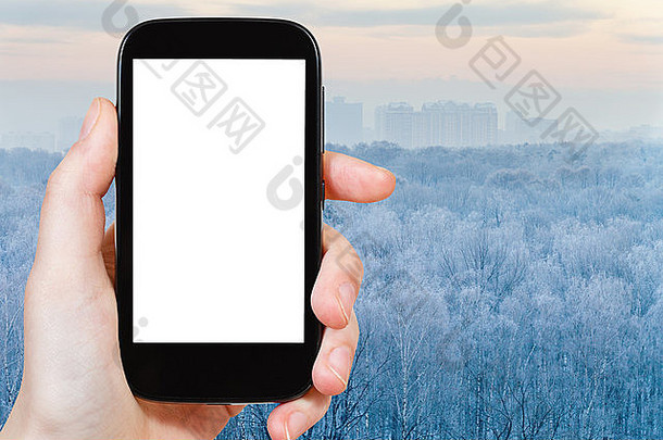 旅游概念-手持智能手机，屏幕切割，背景为冰冻的冬季森林