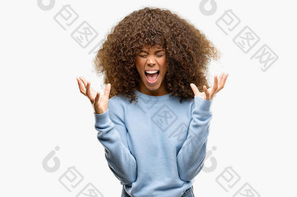 一位非洲裔美国妇女穿着一件毛衣，高举双臂，闭上眼睛，兴奋地尖叫着庆祝疯狂和疯狂的成功。赢家概念