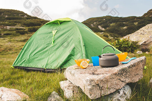 日出时，在草地上用茶壶和帽子露营。保加利亚的山脉。