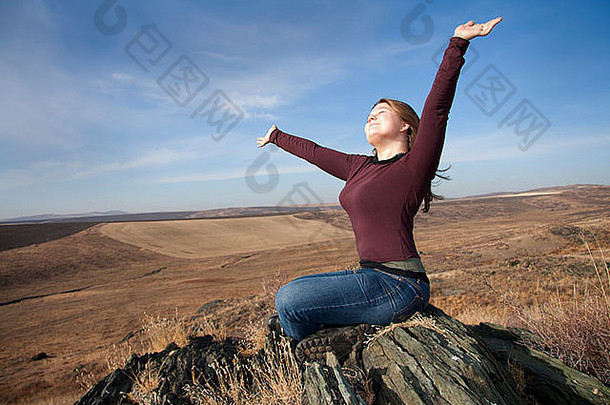 这个女人坐在石头上，双臂举向天堂。