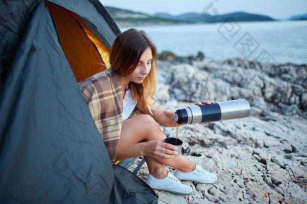 那个女孩坐在帐篷里，小心翼翼地把热水瓶里的茶倒进铁杯里。