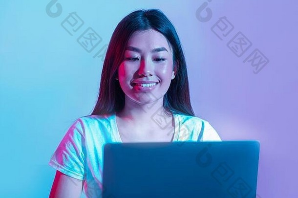 在电脑前工作或玩耍。微笑的亚洲女孩看着霓虹灯下的笔记本电脑