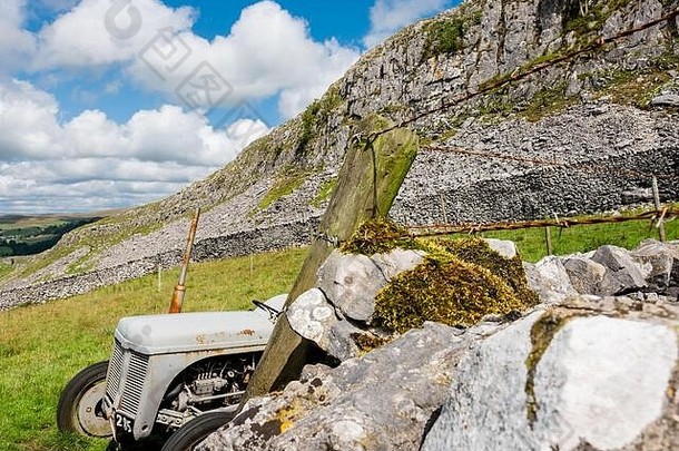 废弃的老式拖拉机出现在山谷中高高的岩壁边界。几年未使用，背景显示剪切岩面。