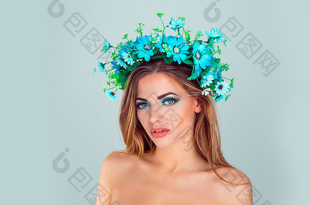 艺术的绿色妆容，美丽的模特。拥有完美皮肤的美女看着摄像机摆出的肩膀，头上戴着花环，头上戴着蓝色的花