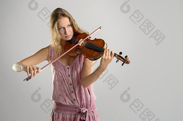 在学院举行的古典独奏会上，身着时尚粉色套装的年轻漂亮女小提琴手站着拉小提琴