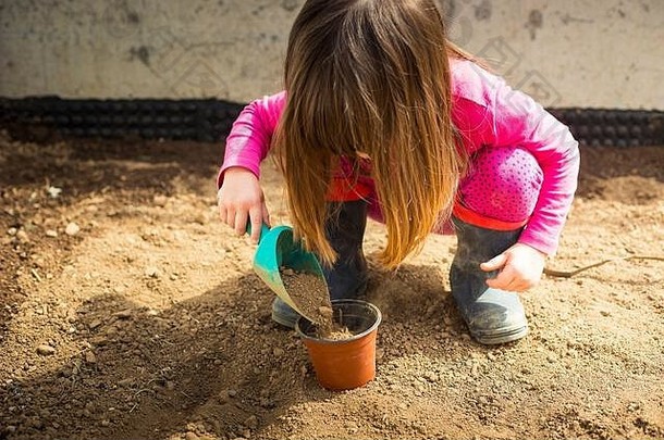 小白种女孩，在她的花园里，在CoVID-19锁定期间用勺子填满一个罐子。潘德米儿童家庭户外创意活动