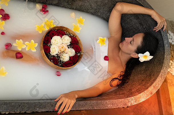 年轻的女人放松黑色的石头浴热带花玫瑰花瓣皮肤治疗奢侈品水疗中心概念