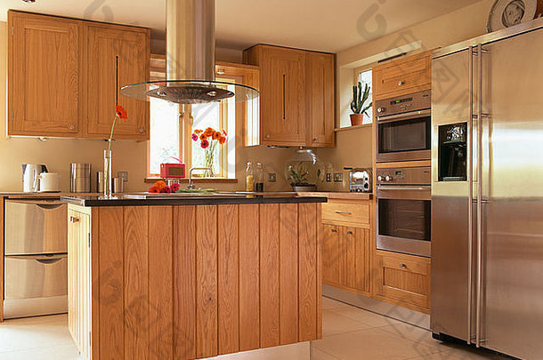 现代厨房中岛式装置上方的提取器，配备木制装置和大型不锈钢美式冰箱