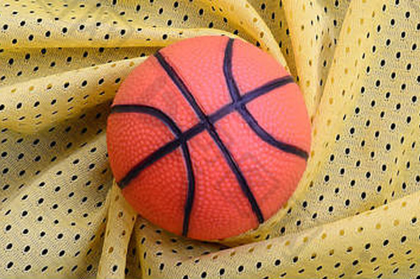 小橙色橡胶篮球位于黄色运动衫上，服装面料纹理和背景有许多褶皱。
