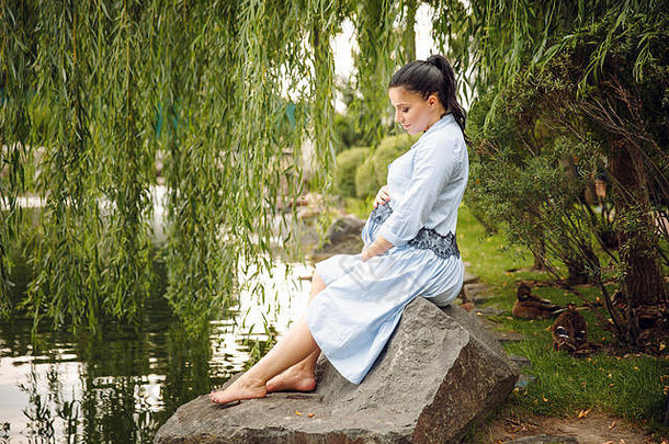 年轻的美丽的怀孕了女人放松岩石湖背景夏天