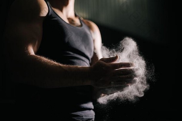 无法辨认的强壮男子用滑石粉拍手准备在健身房锻炼的特写镜头。