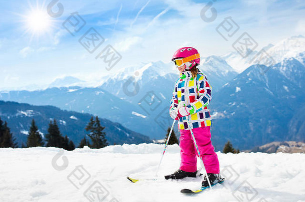 孩子们在山上滑雪。带安全帽、护目镜和杆子的活泼幼儿。幼儿滑雪比赛。家庭冬季运动。儿童滑雪