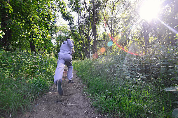 一个穿着灰色运动服的年轻人在森林里的树林中沿着小路跑。户外慢跑运动。运动效应