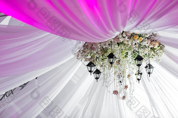 用玫瑰和白花做成的枝形吊灯悬挂在轻型帐篷下。装饰灯