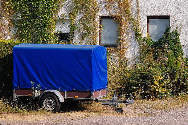 一辆蓝色的旧拖车停在一座常春藤环绕的老房子旁边