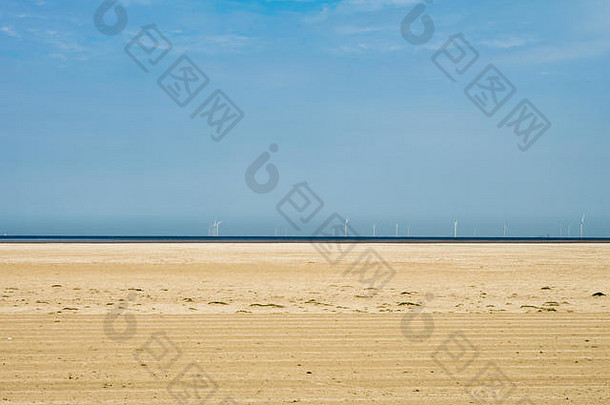 空荡荡的海滩上有风力涡轮机，金色的沙滩和蔚蓝的天空