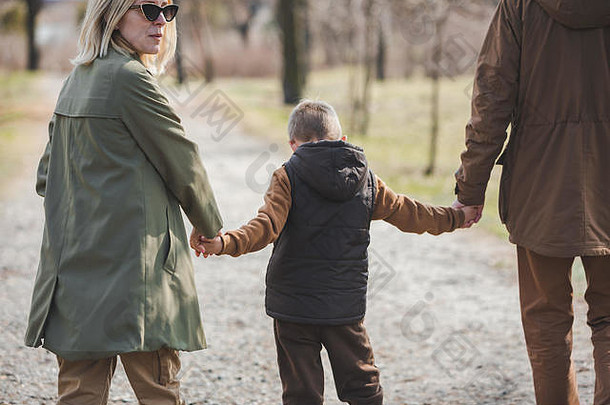 年轻美丽的一家人手牵着手在城市公园散步