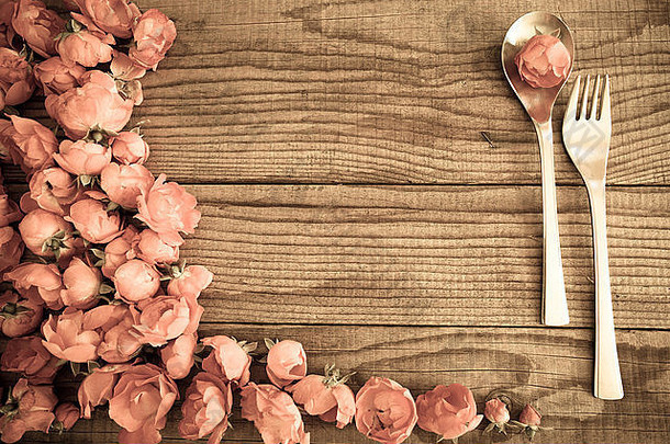 用勺子和叉子在一张木桌子上放上红玫瑰，复古效果