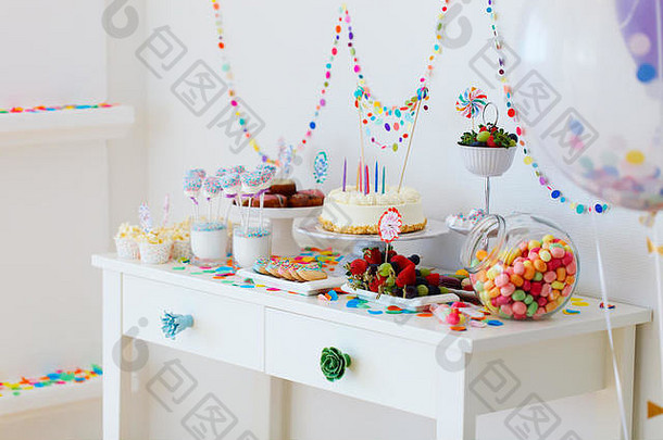 在孩子们的生日聚会上，甜点桌上摆着蛋糕、糖果、棉花糖、棒棒糖、水果和其他糖果