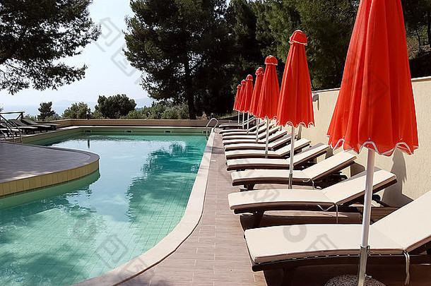 希腊哈尔基迪基，卡斯桑德拉——2012年5月10日：希腊哈尔基迪基，卡斯桑德拉，克朗威尔·拉奥尼公园酒店的游泳池和红色雨伞。