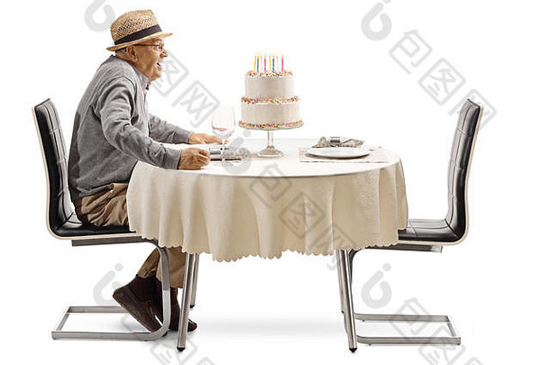 一位兴奋的老人拿着生日蛋糕坐在一张白色背景的<strong>餐厅</strong>餐桌旁