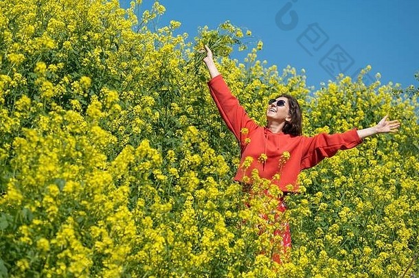 一位年轻女子在一片鲜花盛开的田野里嗅着花香，很高兴。一片美丽的田野，有高大的植物和黄色的花朵。
