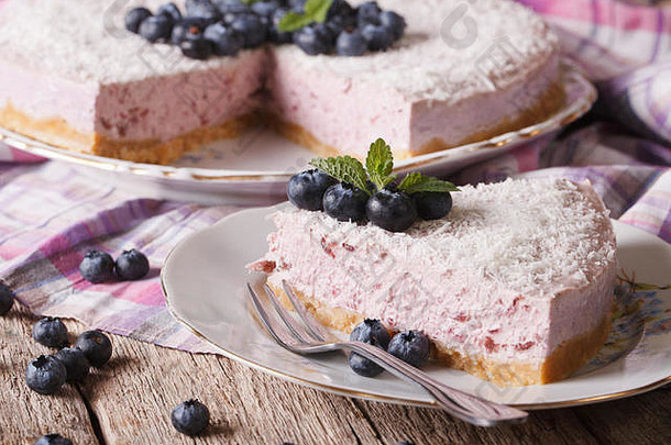 在盘子上切一片美味的蓝莓芝士蛋糕，配上新鲜浆果和椰子特写镜头。水平的