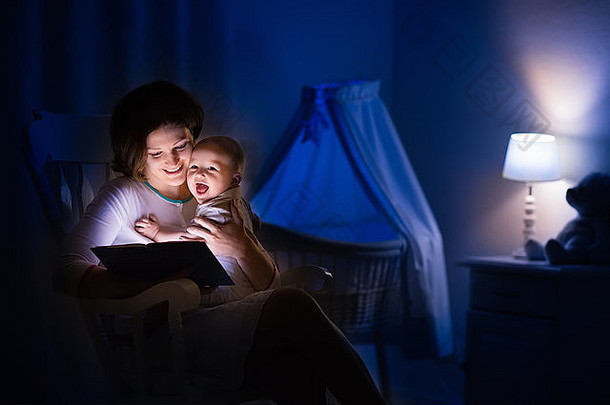 母亲和婴儿在黑暗的卧室里看书。妈妈和孩子在睡觉前看书。晚上和家人在一起。