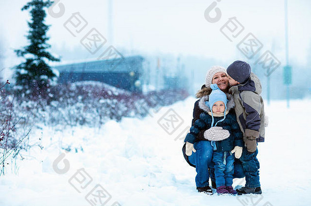 带着两个孩子的年轻母亲在美丽的冬日下雪