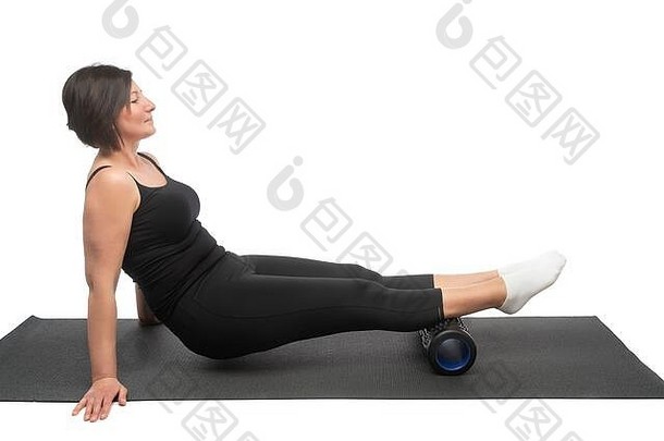 一位中年妇女坐在体操垫上，用肌筋膜滚轮在白色背景上锻炼臀部。