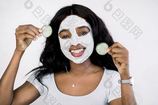 年轻的非洲女人在她的脸上焕然一新的黄瓜面膜，为年轻美丽的皮肤和放松，举行新鲜黄瓜