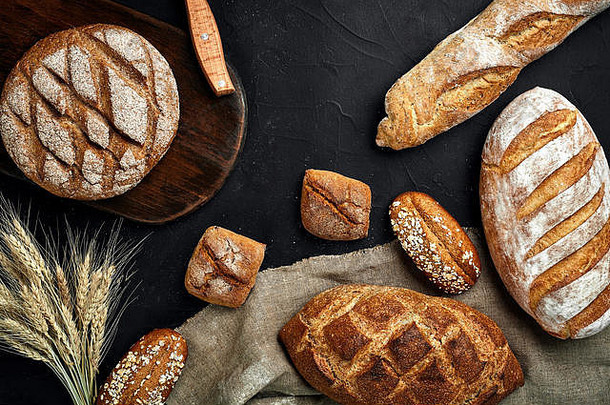 面包店-黑色黑板背景上的金色乡村硬皮面包和小面包。