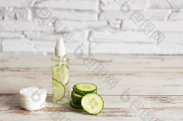 清爽面部黄瓜爽肤水，瓶内有绿色黄瓜片和棉垫，白色木质背景。复制空间。