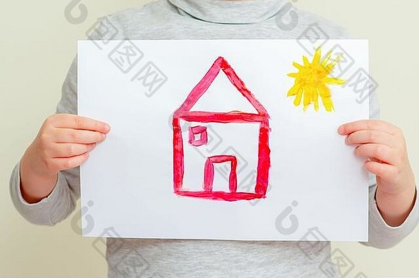 这个孩子的特写镜头是拿着一张小学里有太阳的红房子的照片。绘画观念。