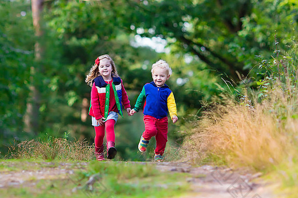 孩子们在秋天公园玩耍。在一个阳光明媚的秋天，孩子们在户外玩耍。男孩和女孩手拉手在森林里奔跑。