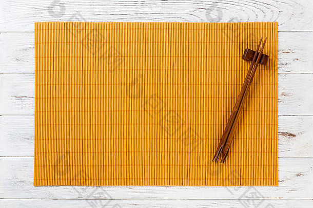 两个寿司筷子，白色木质背景上有空的黄色竹垫或木板，带有复印空间。空的亚洲食物背景。