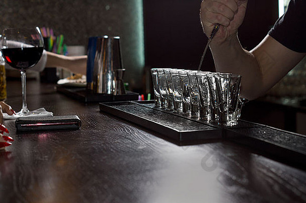 酒吧柜台上的一排玻璃杯，一名酒吧招待用手臂在其中一个玻璃杯内搅拌酒精