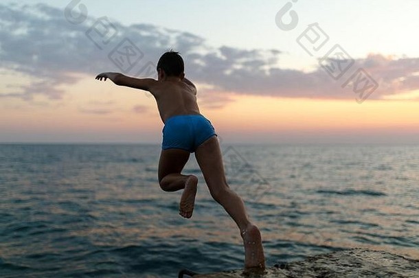 在美丽的夏日日落的背景下，少年从码头跳入大海。