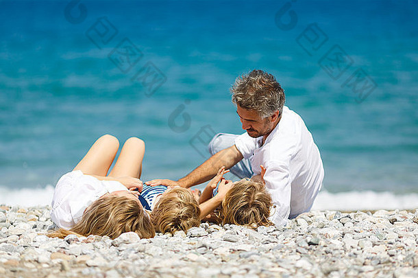 有两个孩子躺在海滩上的幸福家庭
